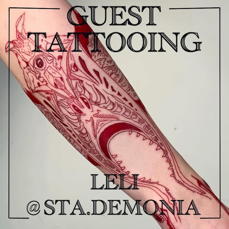 En fineline tatuering i rött bläck av ett alienliknande monster över underarm. Av queer gästtatuerare Leli Bolondi