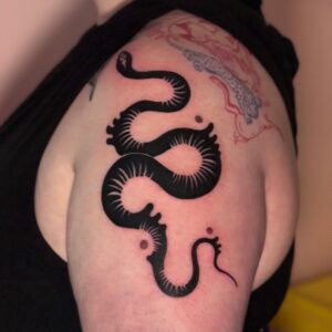 Tatuering i form av orm som slingrar över arm och axel, i blackwork stil av queer tatuerare Tere Falomir.