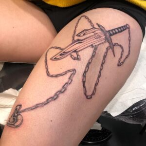 Tattoo in blackwork style over a leg. A big knife with a chain running from the handle with a shiny heart in the end. By queer tattooer Bahi. 