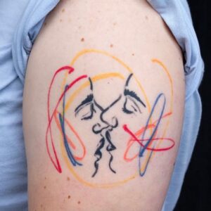Too faces about to kiss, tattoo on upper arm by tattooer Cee Burgundy.