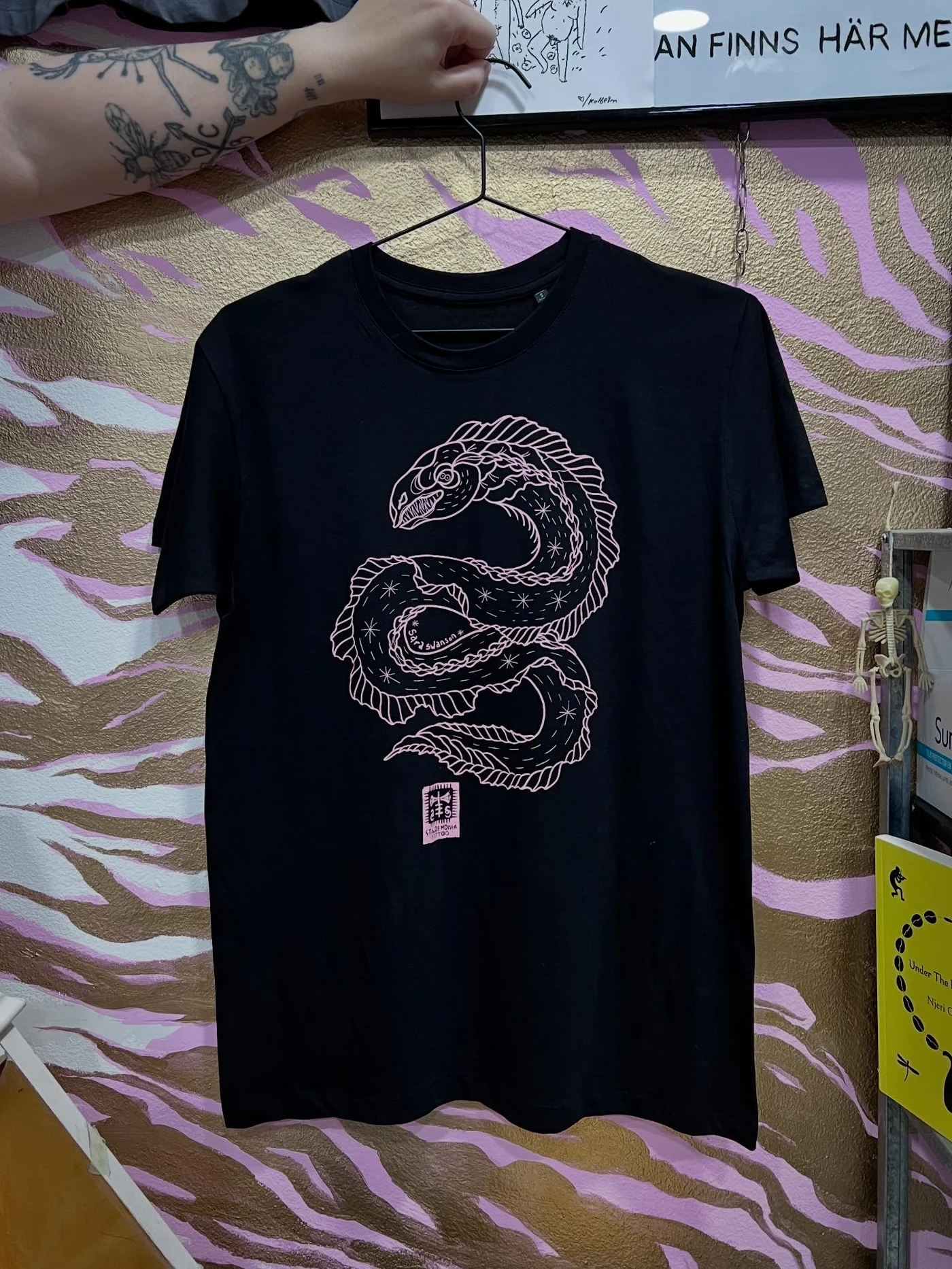 Pink eel on a black T-shirt in line tattoo style, by queer tattooer Sara Swanson